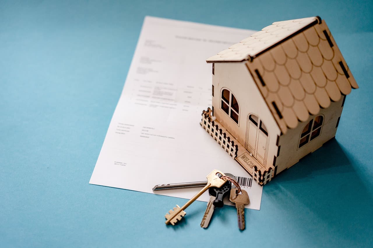 House keys and a small wooden house resting on mortgage paperwork